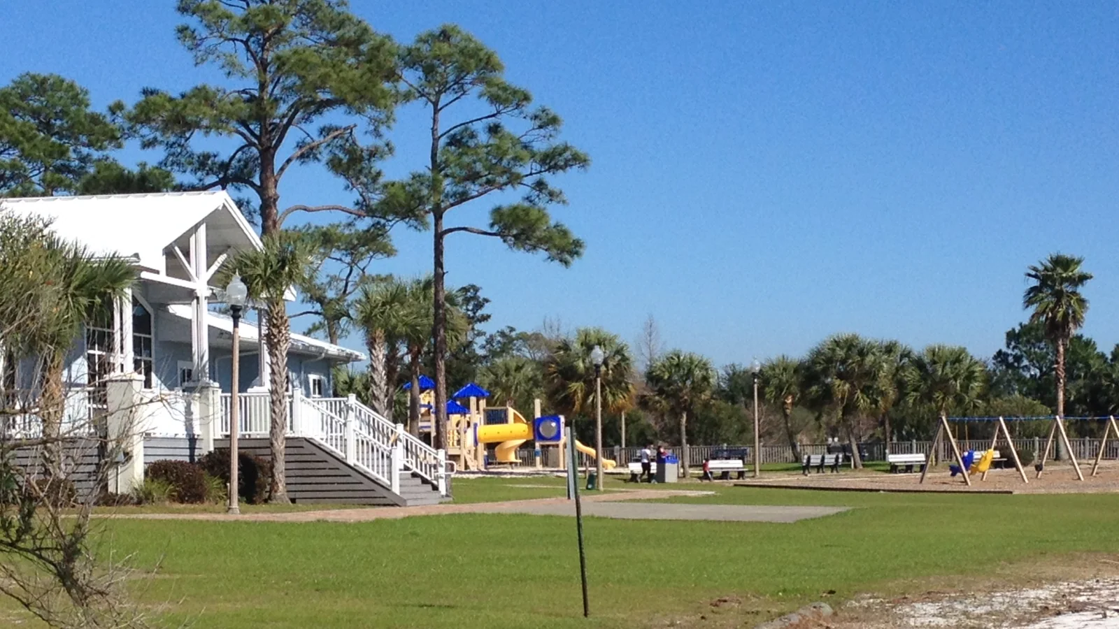 Green lawn meeting pale sandy soil near palms, pines, and a white park building in Navarre, Florida
