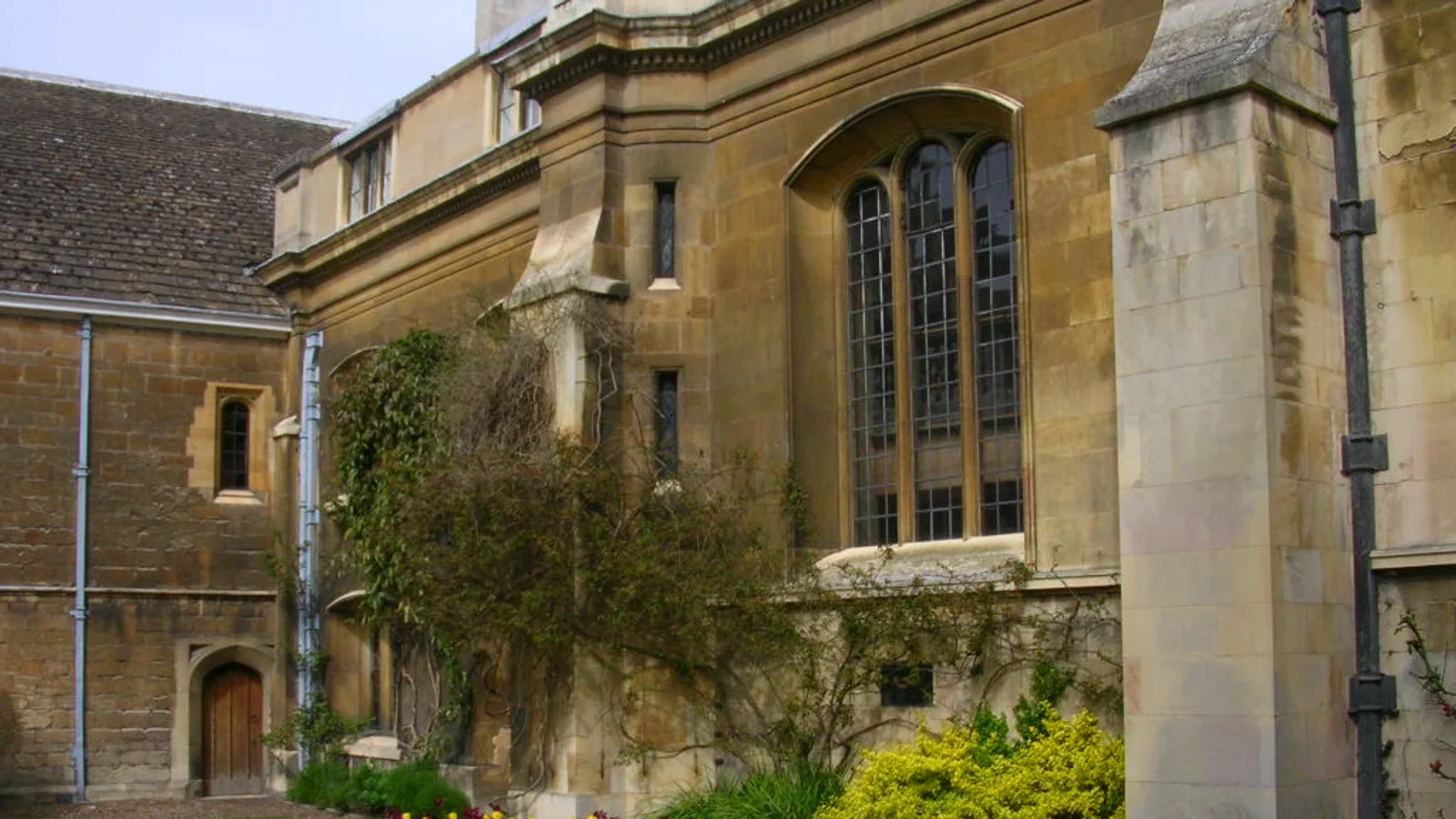 A curved flower bed borders a neatly cut lawn beside a stone building.